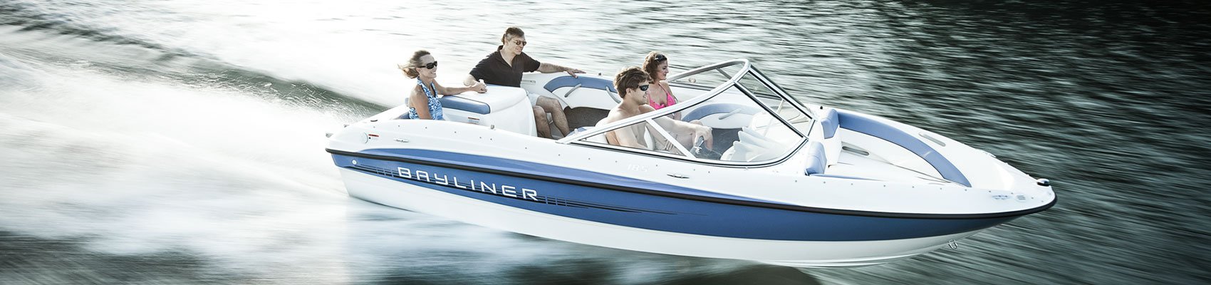 A white and blue Bayliner boat speeding across the water, leaving a wake.