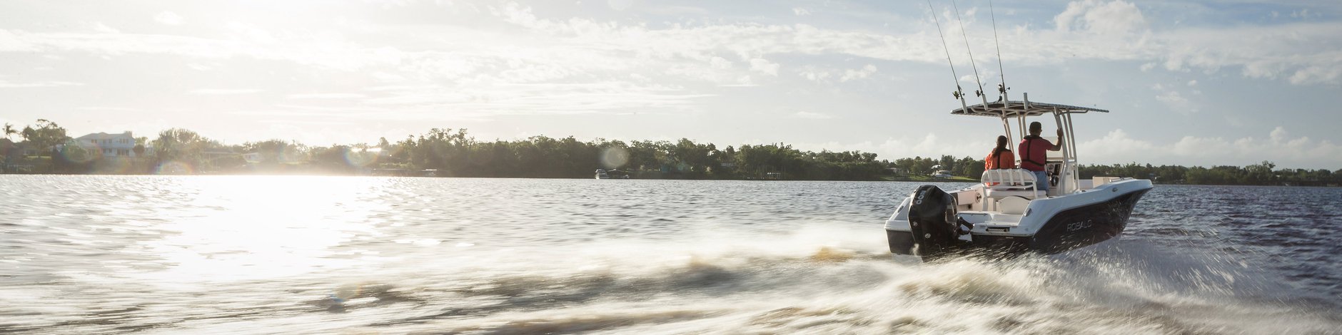 A fishing boat with two people speeding across water, leaving a wake, with a bright sun in the background.