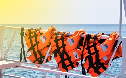 Safety bright orange life jackets hanging on a white railing